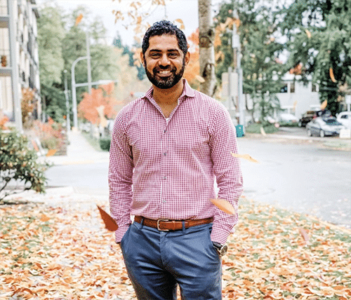 Dr. Kunal Narang, a dentist in redmond, standing outside in a causal red checkered shirt and blue slacks, smiling at the camera.