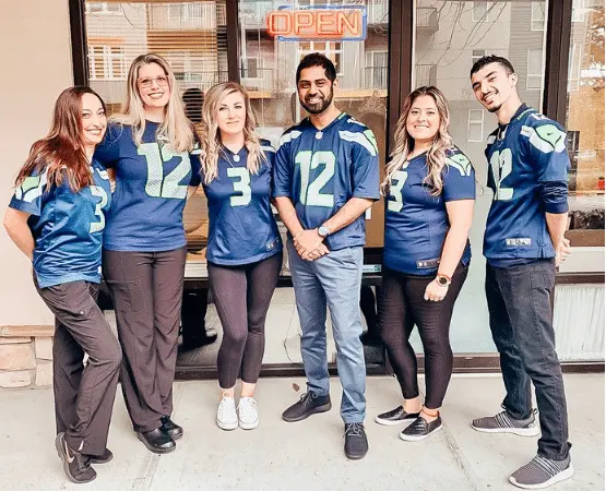 The dental team of Sunrise Dental of Redmond standing in front of the dentist office wearing Seattle Seahawk jersey's